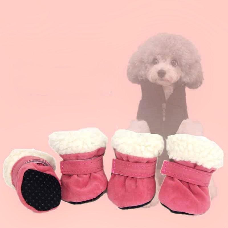 Pink dog boots with white fleece lining and black soles displayed in front of a small poodle wearing a black outfit on a pink background